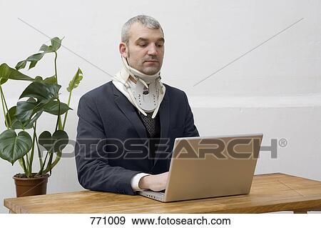 A businessman with a neck brace working on a laptop View Large Photo Image Stock Photo - A businessman with a neck brace working on a laptop. Fotosearch