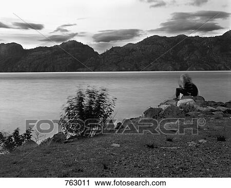 A person sitting at the edge of a lake View Large Photo Image Stock Image - A person sitting at the edge of a lake. Fotosearch