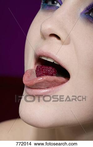 Picture - A woman holding a raspberry on her tongue. Fotosearch