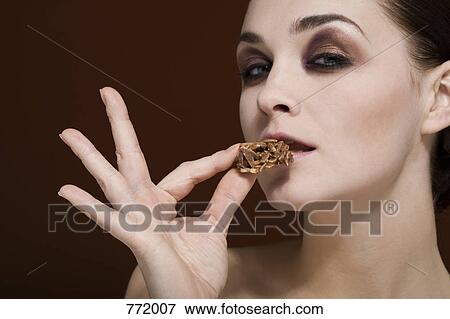 A woman holding an almond chocolate cluster to her mouth View Large Photo Image Stock Photo - A woman holding an almond chocolate cluster to her mouth. Fotosearch