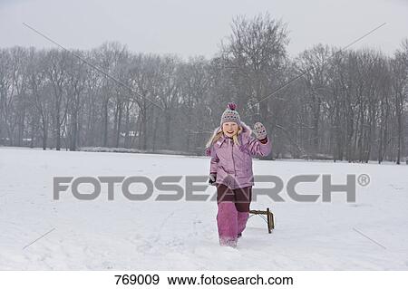 Stock Photo - A young girl pulling a sled and waving. Fotosearch