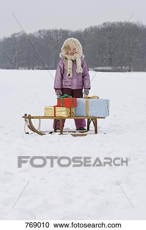 Stock Image - A young girl with a sled with presents. Fotosearch