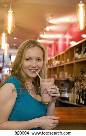 A young woman sitting in a cafe and holding a fruit smoothie View Large Photo Image Picture - A young woman sitting in a cafe and holding a fruit smoothie. Fotosearch