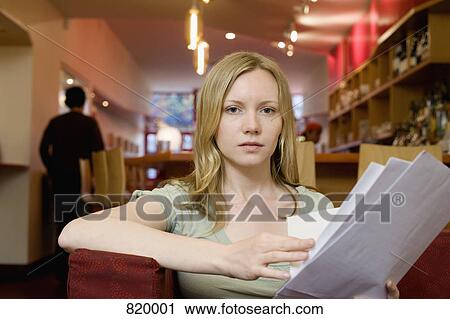 Stock Image - A young woman sitting in a cafe and looking at the menu. Fotosearch