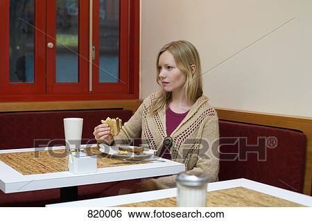 A young woman sitting in a cafe and eating a toasted sandwich View Large Photo Image Stock Photograph - A young woman sitting in a cafe and eating a toasted sandwich. Fotosearch