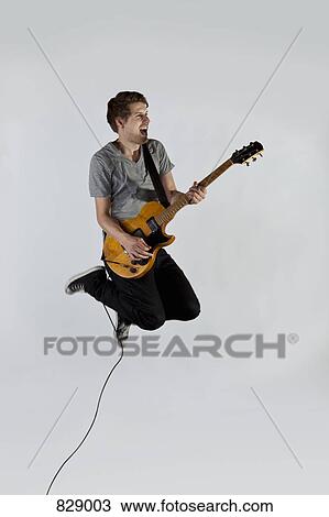 Stock Image - A musician playing a guitar and jumping in mid-air. Fotosearch