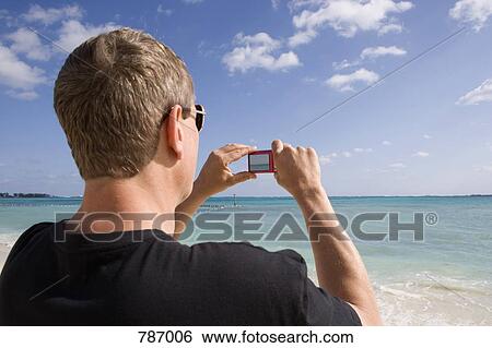 Rear view of a man using a digital camera, Cable Beach, Nassau, Bahamas, Caribbean View Large Photo Image Stock Photograph - Rear view of a man using a digital camera, Cable Beach, Nassau, Bahamas, Caribbean. Fotosearch