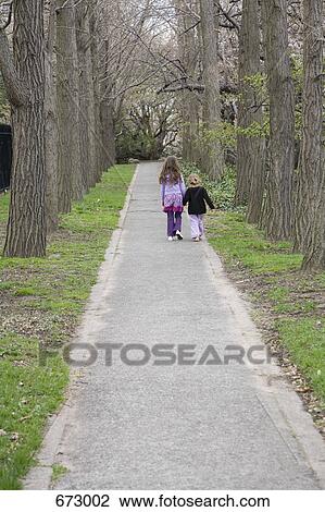 Two young girls holding hands and walking down a path, rear view View Large Photo Image Stock Image - Two young girls holding hands and walking down a path, rear view. Fotosearch