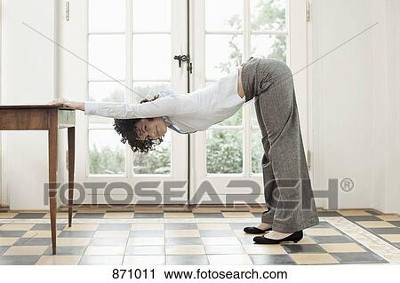 Stock Image - A businesswoman stretching against a table. Fotosearch