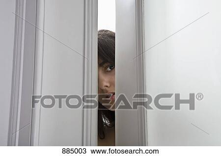 Stock Image - A woman peeking through a cracked door. Fotosearch