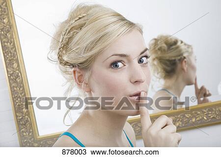 A woman with her finger to her lips in front of a mirror, looking at camera View Large Photo Image Stock Image - A woman with her finger to her lips in front of a mirror, looking at camera. Fotosearch