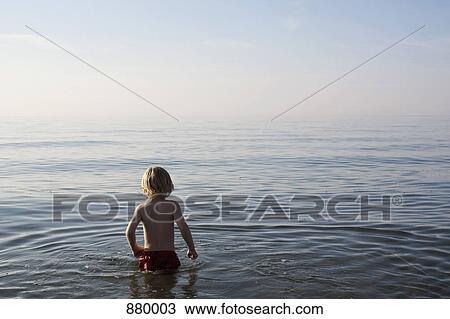 Stock Image - A young boy standing in the sea. Fotosearch