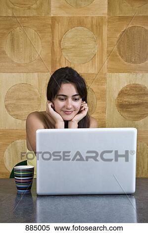 A young woman sitting at a marble table using a laptop View Large Photo Image Stock Photography - A young woman sitting at a marble table using a laptop. Fotosearch