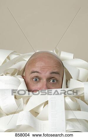 Picture - Detail of a man buried in printed receipts. Fotosearch