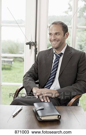 Portrait of a businessman sitting at a table and looking away View Large Photo Image Stock Image - Portrait of a businessman sitting at a table and looking away. Fotosearch
