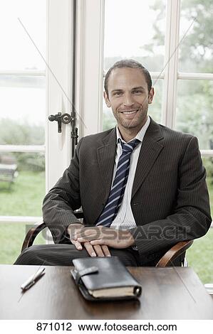 Portrait of a businessman sitting at a table View Large Photo Image Stock Image - Portrait of a businessman sitting at a table. Fotosearch