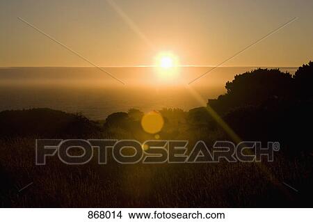 View of the sun rising over the sea and a grassy field View Large Photo Image Picture - View of the sun rising over the sea and a grassy field. Fotosearch