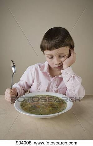 Stock Photo - A boy looking disappointedly at a bowl of vegetable soup. Fotosearch