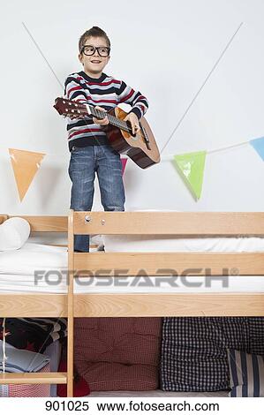 Stock Photography - A boy standing on a bunk bed playing with a guitar. Fotosearch