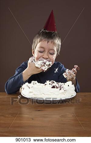 A boy wearing a party hat eating birthday cake with his hands, studio shot View Large Photo Image Stock Image - A boy wearing a party hat eating birthday cake with his hands, studio shot. Fotosearch