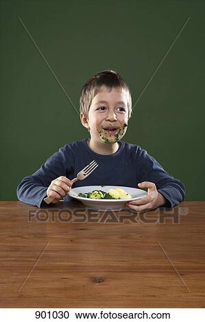 Stock Image - A cheerful boy getting food all over his face while eating, studio shot. Fotosearch