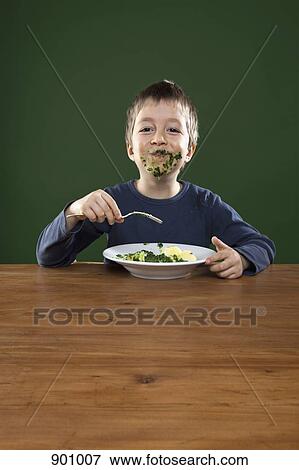 Stock Photo - A cheerful boy getting food all over his face while eating, studio shot. Fotosearch