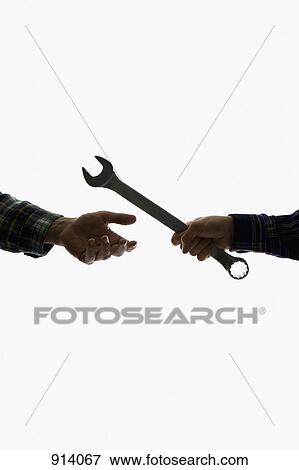 Stock Photo - A construction worker handing a wrench to another worker, focus on hands. Fotosearch