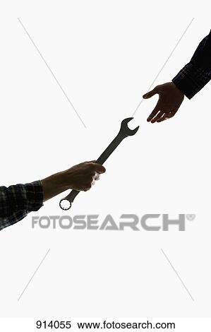 Stock Photography - A construction worker handing a wrench to another worker, focus on hands. Fotosearch