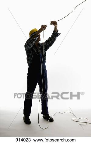 Stock Image - A construction worker putting a plug into an extension cord. Fotosearch