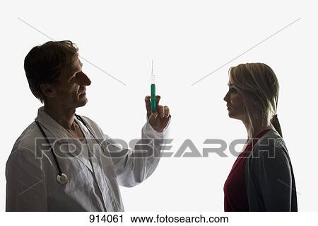 A doctor holding up a syringe facing a worried patient View Large Photo Image Stock Image - A doctor holding up a syringe facing a worried patient. Fotosearch