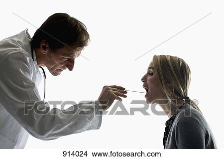 Picture - A doctor using a tongue depressor performing an exam on a patient. Fotosearch