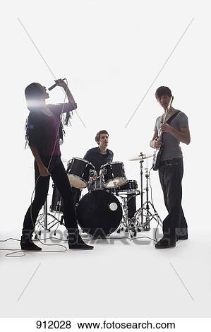Stock Photo - A drummer, guitarist and singer performing, studio shot, white background, back lit. Fotosearch