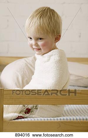 A happy baby boy wrapped in a towel sitting on a bed View Large Photo Image Stock Photograph - A happy baby boy wrapped in a towel sitting on a bed. Fotosearch