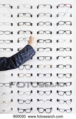 Stock Image - A human hand choosing a pair of glasses in an eyewear store. Fotosearch