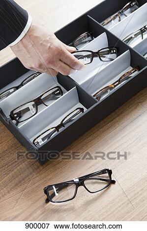 Stock Photo - A human hand choosing a pair of glasses in an eyewear store. Fotosearch