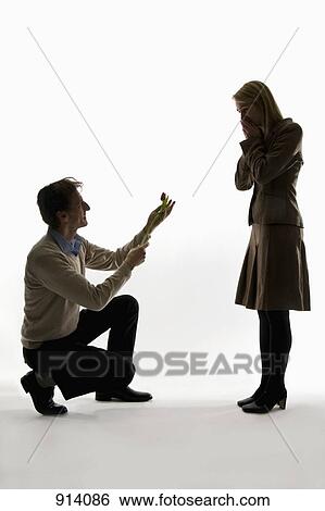 A man kneeling, presenting a flower to his surprised girlfriend View Large Photo Image Stock Photograph - A man kneeling, presenting a flower to his surprised girlfriend. Fotosearch