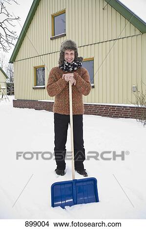 Picture - A man leaning on a snow shovel preparing to shovel snow. Fotosearch