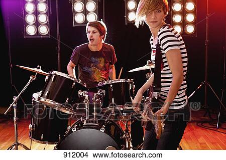 A man playing drums and a woman playing guitar performing on stage in a rock band View Large Photo Image Picture - A man playing drums and a woman playing guitar performing on stage in a rock band. Fotosearch