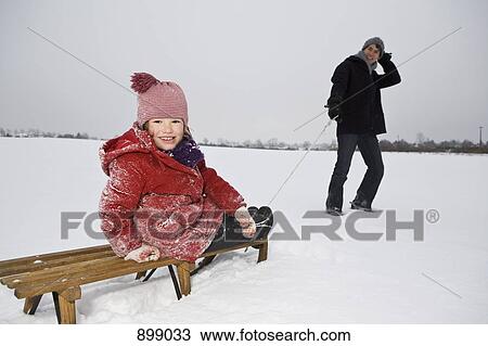 Stock Image - A man pulling a sled daughter on it. Fotosearch