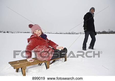 Stock Photo - A man pulling a sled daughter on it. Fotosearch
