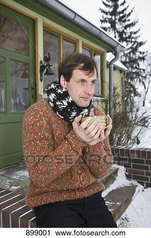 Stock Image - A man sitting on the front stoop of a house holding a hot drink. Fotosearch