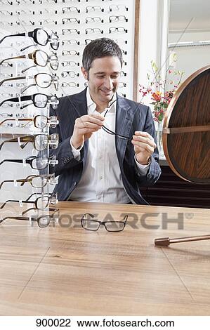 Stock Image - A mature man choosing a pair of eyeglasses in an eyewear store. Fotosearch