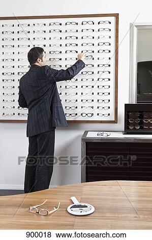 Stock Photo - A mature man choosing a pair of eyeglasses in an eyewear store. Fotosearch
