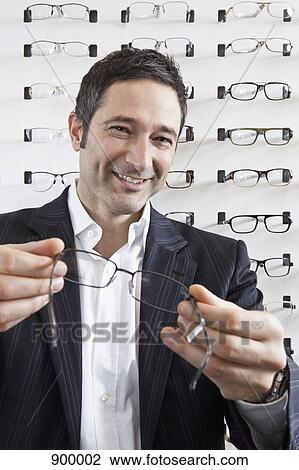 A smiling optician holding up a pair of glasses to the camera in an eyewear store View Large Photo Image Stock Image - A smiling optician holding up a pair of glasses to the camera in an eyewear store. Fotosearch