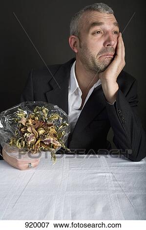 Stock Photo - A well-dressed man holding a bouquet of dead flowers and crying. Fotosearch
