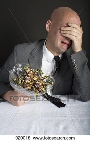 Stock Photo - A well-dressed man holding a bouquet of dead flowers and crying. Fotosearch