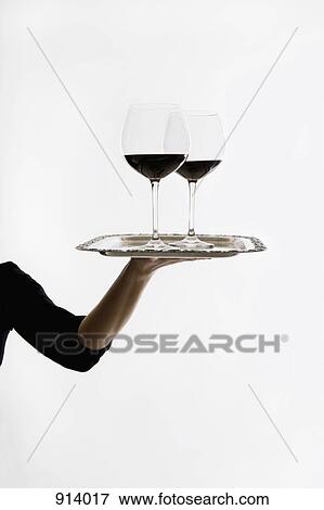 Stock Photo - A woman carrying two of glasses of red wine on a tray. Fotosearch