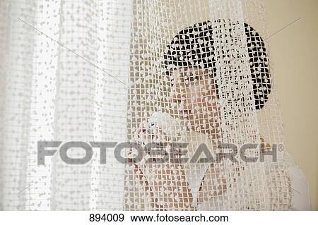 Stock Photo - A woman holding a cup looking through a window. Fotosearch