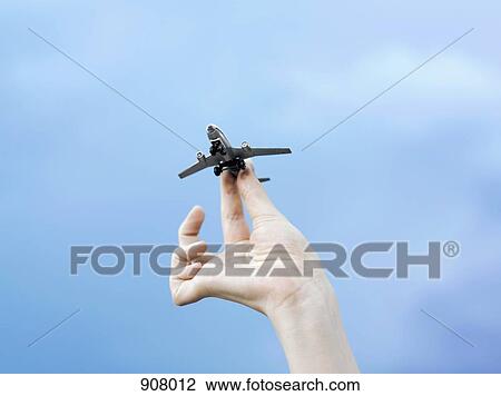 Stock Image - A woman holding a model airplane, detail of hand, low angle view. Fotosearch
