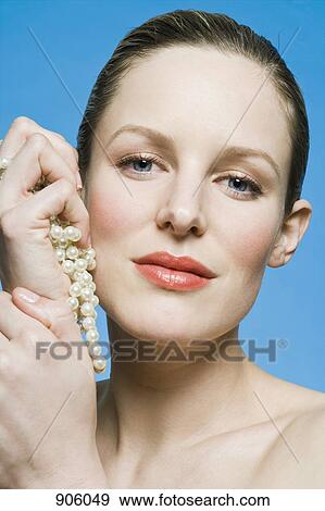 Stock Photo - A woman holding pearls, head and shoulders, portrait. Fotosearch